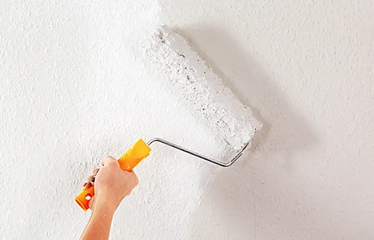 Malerbedarf für Innen- und Außenarbeiten – Farbroller beim Streichen einer Wand