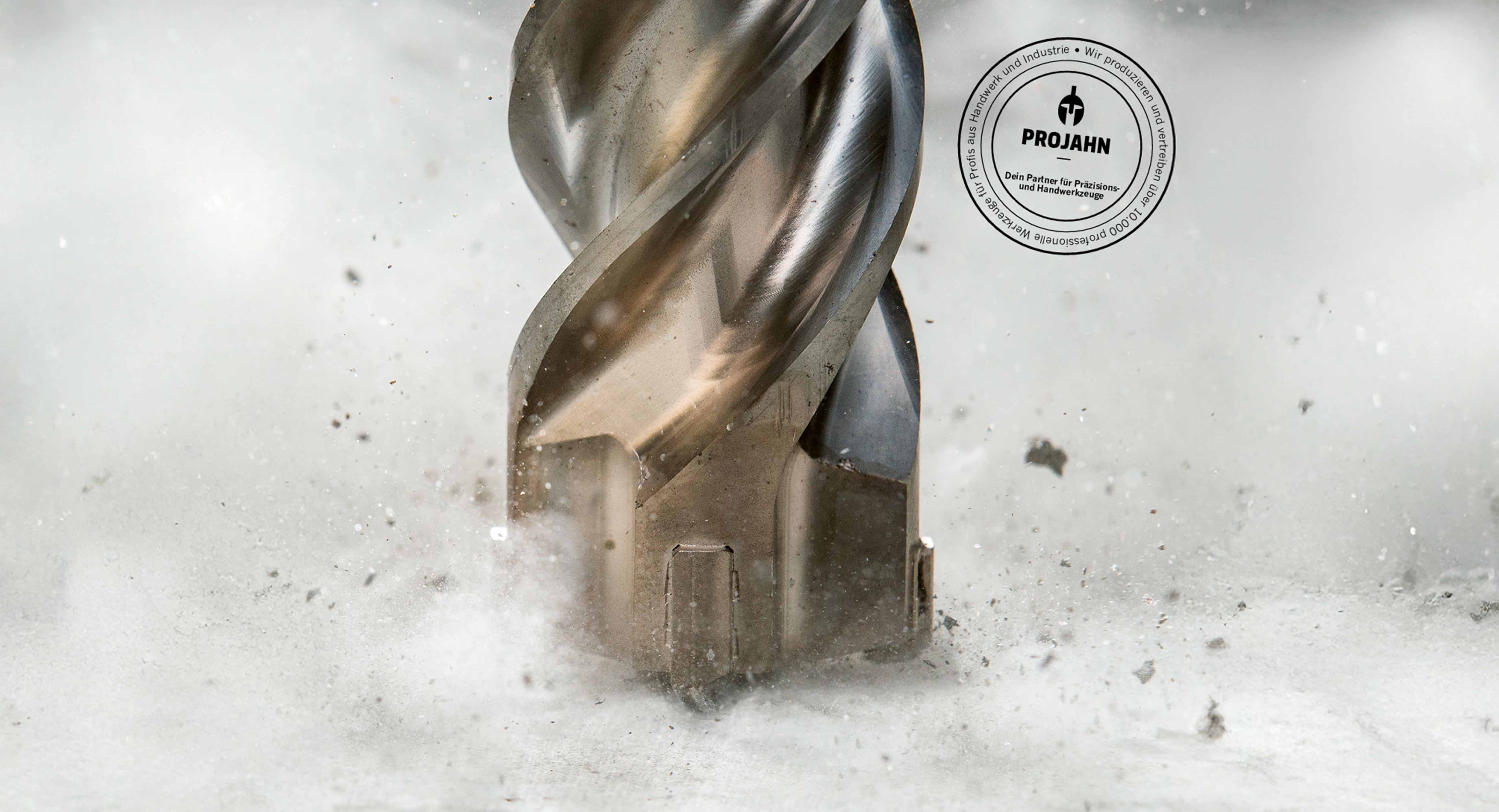 Nahaufnahme eines rotierenden Metallbohrers der Marke PROJAHN beim Bohren in Beton, mit Funken und Staub – Präzisionswerkzeuge für Handwerk und Industrie in Plettenberg.